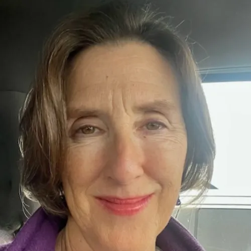 A middle-aged woman with short brown hair and a slight smile looks at the camera inside a vehicle.